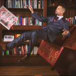 A man in a suit looks like he is floating in the air in front of a bookcase.